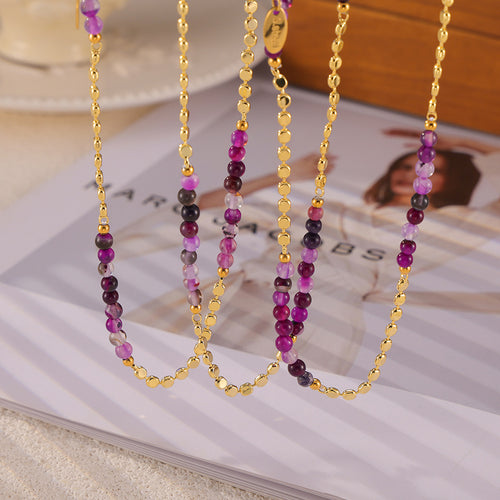 Several gold disc and purple agate bead necklaces draped over a fashion magazine