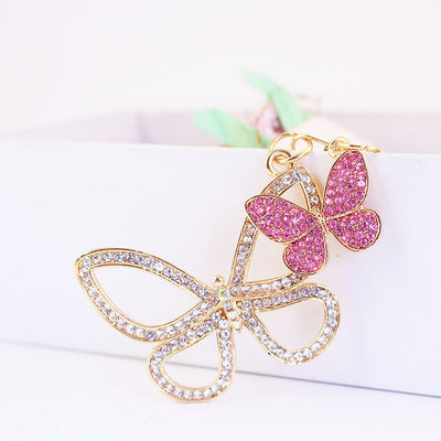 Pink rhinestone butterfly hangs above a larger clear open-wing butterfly.