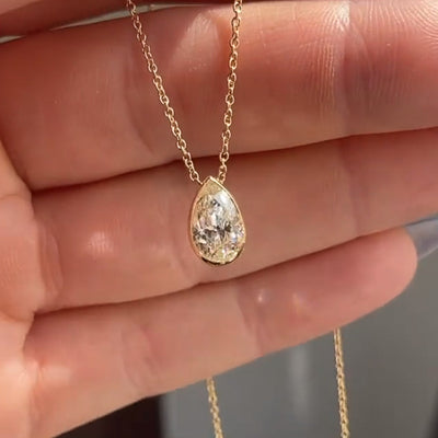 Gold tone pear bezel clear crystal pendant held in open palm