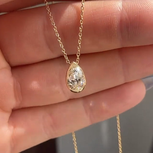 Gold tone pear bezel clear crystal pendant held in open palm