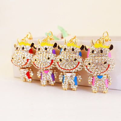 Four gold-tone cow keychains with clear stones and red, purple, blue, and pink accents.