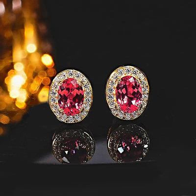 Gold oval red halo CZ stud earrings on dark reflective surface bokeh lights
