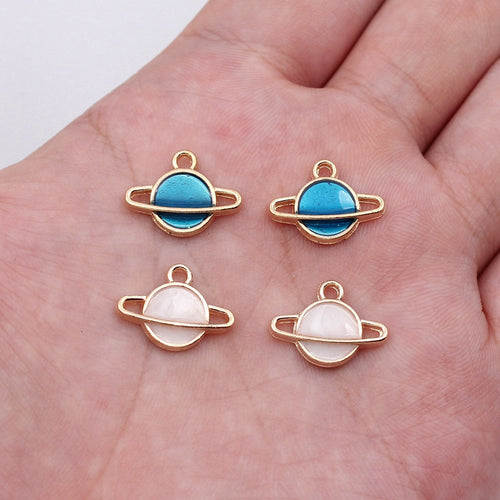 Ringed planet enamel charms shown on a hand for scale