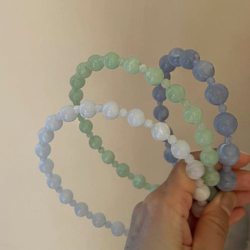 Hand holding blue green and white acrylic bead headbands together