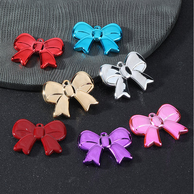 Seven glossy acrylic bow charms in red, blue, silver, gold, dark red, purple and pink arranged on leather and slate surf