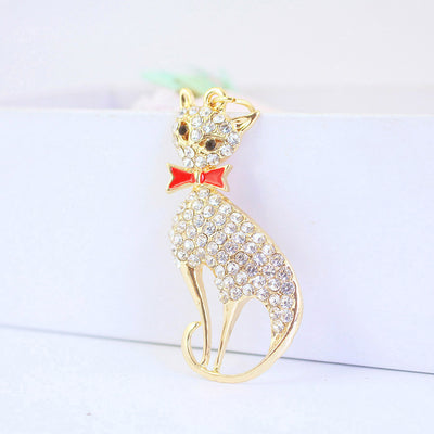 Front view of a gold-tone cat charm with clear stones and a red bow.