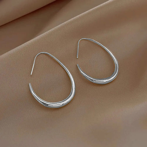 Silver teardrop open drops resting on beige satin fabric