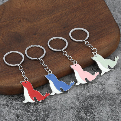 Four seal keychains in red, blue, pink, and light green displayed on wood.