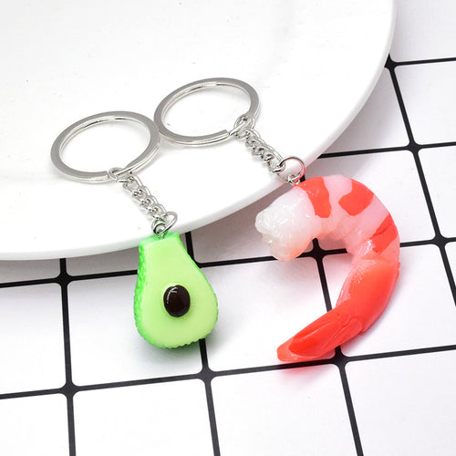 Avocado and shrimp food keychains beside white plate on grid
