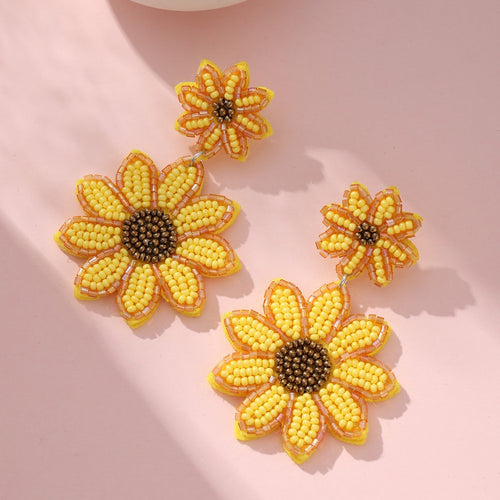 Layered sunflower beaded earrings close up showing bronze bead centers on pink surface