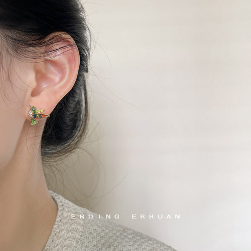 Gold-tone multicolor-enamel hummingbird studs shown worn on an ear.