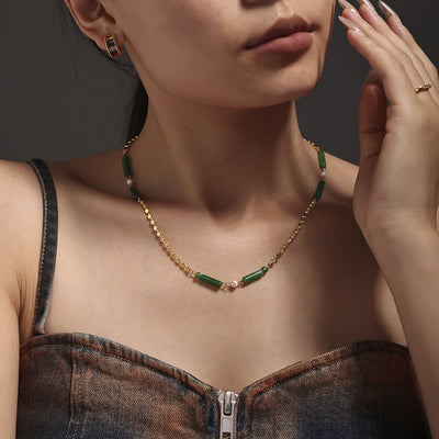 Model wearing gold disc chain necklace with green tube beads at collarbone