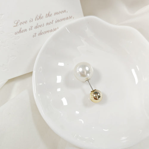 Short pearl and gold ball stick pin brooch on a white dish