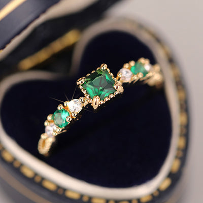 Product view showing gold-tone three-stone ring with square green stones