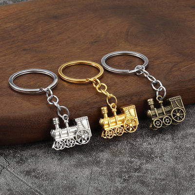 Three locomotive keychains in silver, gold and antique bronze tones on a wooden surface.
