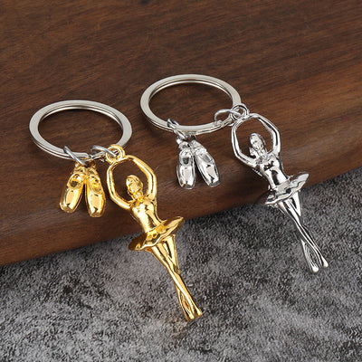 Gold-tone and silver-tone ballerina keychains displayed together on wood and gray fabric.