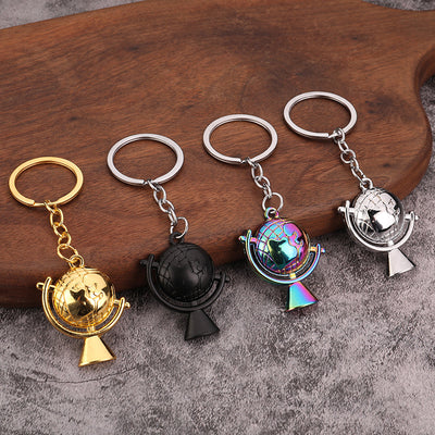 Four globe pendant keychains arranged on a wooden board in gold, black, rainbow, and silver finishes.