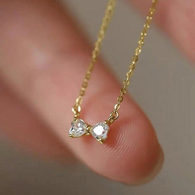 Gold double heart bow pendant held on fingers close-up