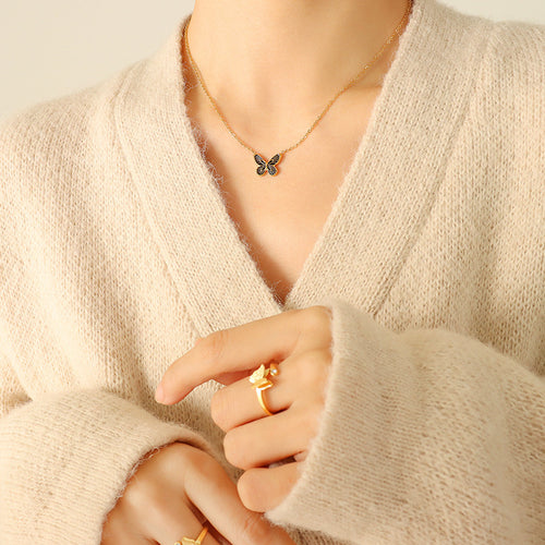 Model in beige cardigan wearing gold black-wing butterfly pendant necklace