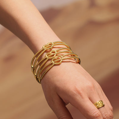 Gold dual-line beaded heart bangles stacked on wrist outdoors