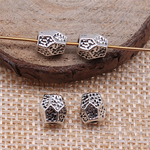 antique silver faceted irregular barrel bead arranged on a round wood display
