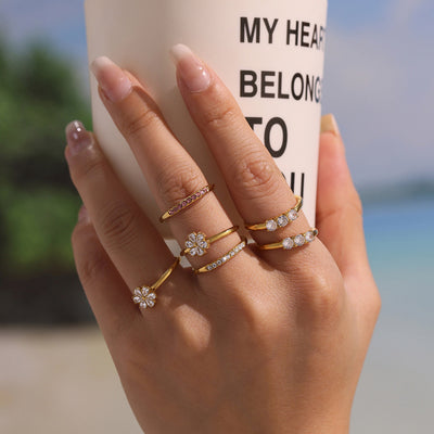 Gold zircon band and flower rings stacked on hand by mug