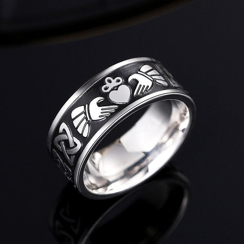 Steel Claddagh band ring on black reflective surface showing heart hands