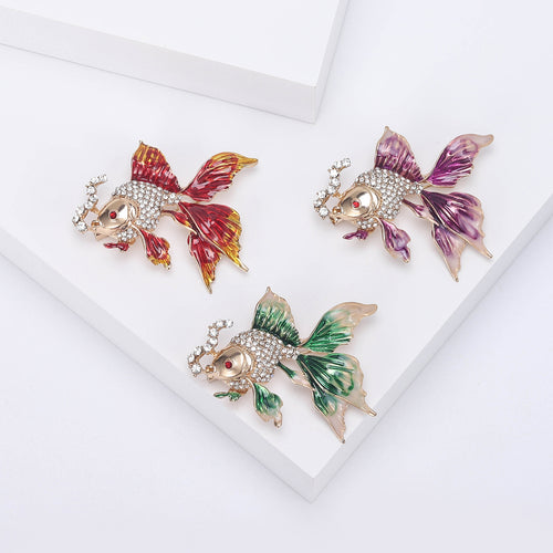 Three goldfish brooches in red, purple, and green enamel on white display
