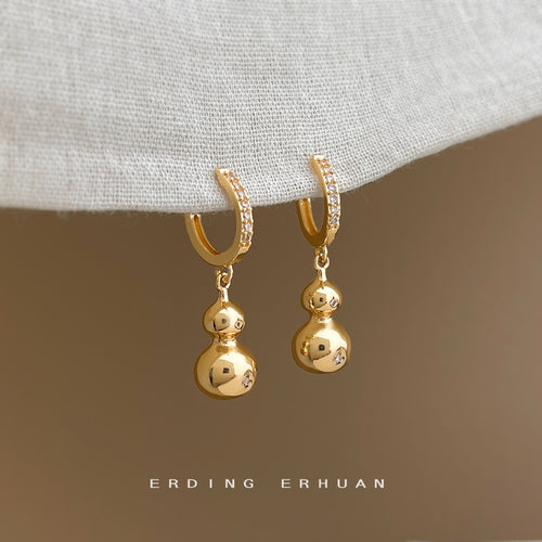 Gold gourd drop huggie hoops hanging from fabric edge