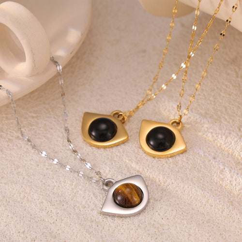 Close-up of gold black-stone and steel tiger-eye eye pendants on beige surface