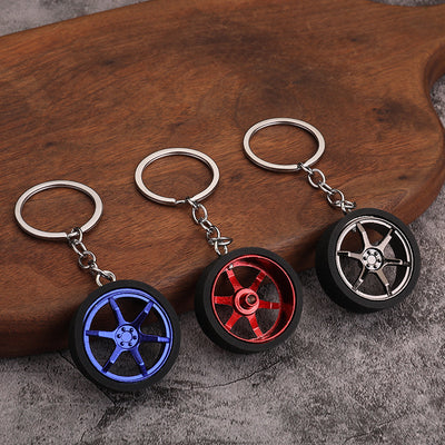 Three wheel-shaped keychains in blue, red, and gunmetal on a wooden surface.