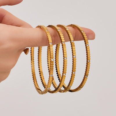 Hand holding stack of gold gear-texture crystal bangles
