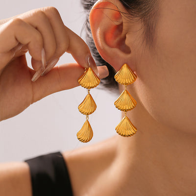 Gold triple shell fan drop earrings worn and held near ear