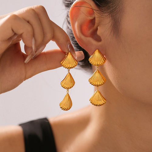 Gold triple shell fan drop earrings worn and held near ear