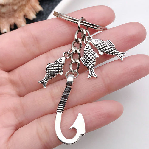 Styled close-up of antique silver angler fish and hook charm keychain showing colors and surface details