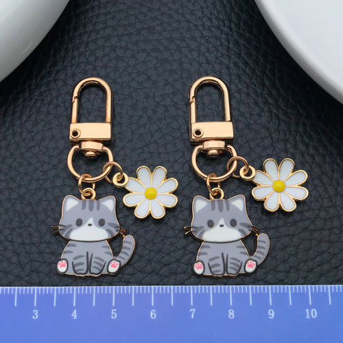 Styled close-up of gray cat and white daisy enamel clip keychain eight-style showing colors and surface details