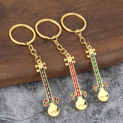 Three gold tone instrument keychains with black, red, and green colored details rest on a wooden surface.