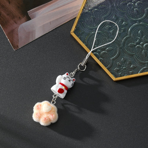 Lucky cat phone strap with peach flocked heart-pad paw on dark surface