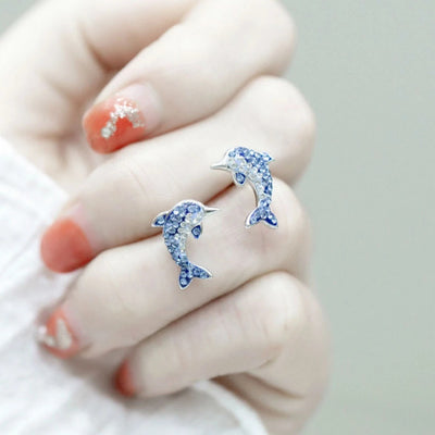 Blue clear pave dolphin stud earrings held between fingers