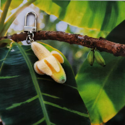Banana plush charm hanging on branch among tropical leaves