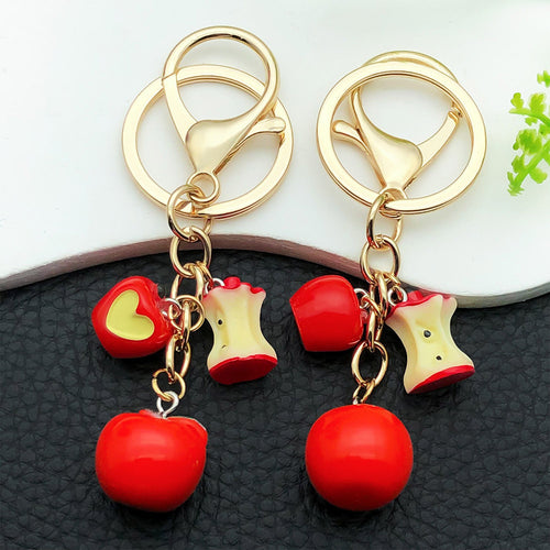 Grouped red apple trio keychain with whole cut and core charms arranged together on a styled display surface