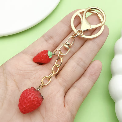Image 1 showing a hand holding a strawberry shaped keychain.