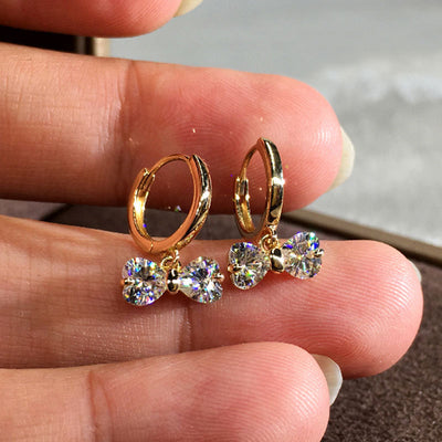 Front view of gold tone huggie earrings with crystal bow drops with clear crystal details