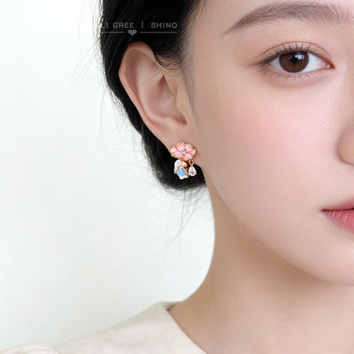 Gold-tone pink-flower blue-green-leaf clear-teardrop studs shown worn on an ear.