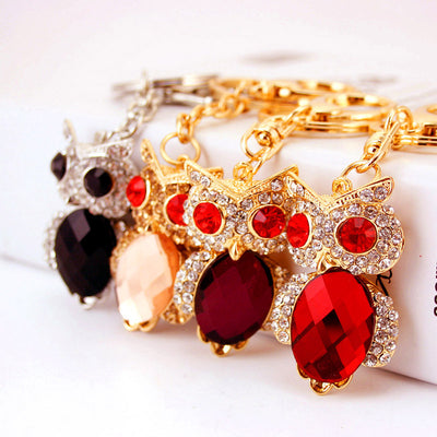 Four owl keychains in red, purple, peach and black displayed in a row.