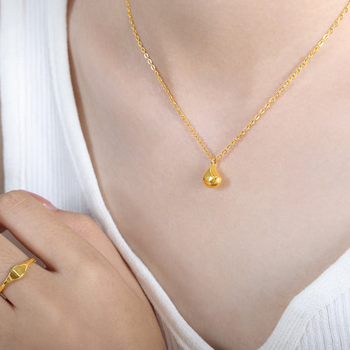 Model wearing gold teardrop pendant necklace on collarbone with white top
