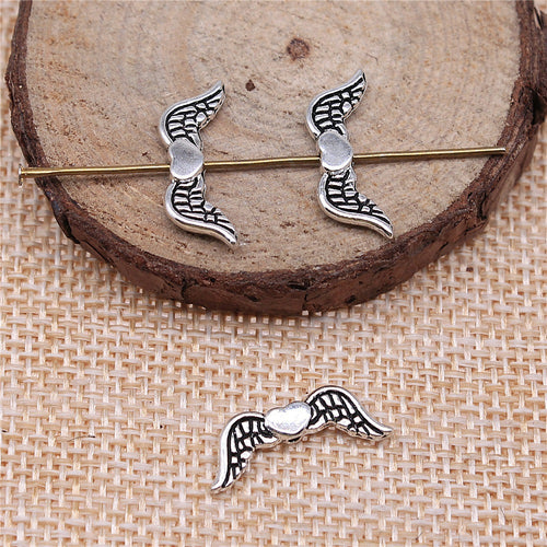 Antique Silver, Antique Gold, Antique Bronze winged-heart small-hole bead displayed on a wood and linen setting
