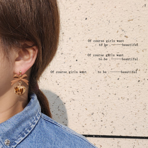 Tan bow leopard pom earring worn on ear