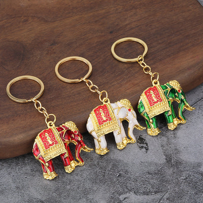 Three elephant keychains in red, white, and green rest on a wooden and gray surface.
