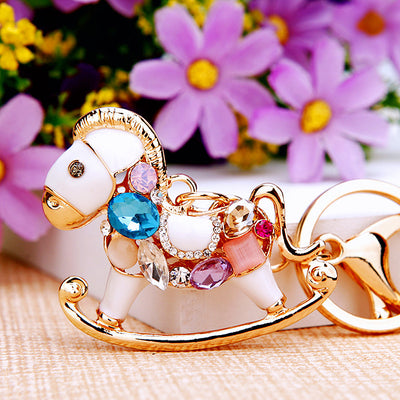 A styled product view shows the jeweled rocking horse keychain and attached key hardware.